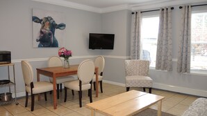Un comedor con mesa y sillas de madera, un florero con flores, un televisor de pantalla plana en la pared y una ventana con cortinas.
