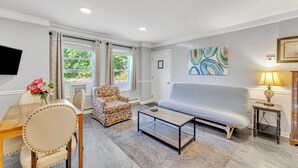 Una sala de estar con sofá, mesa de centro, sillón estampado, mesa de comedor con sillas y televisor.