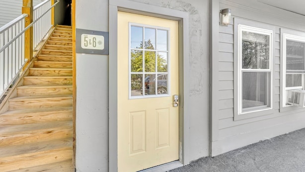 A wooden staircase leading to a yellow door with a window, a number '5&6' sign, and a covered porch area.