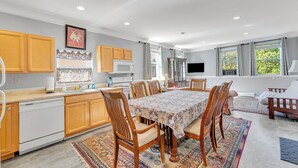 A modern kitchen with wooden cabinets, a dining table with chairs, and a large window providing natural light.