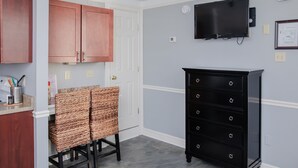 A kitchen with copper cabinets, wicker chairs, a black dresser, and a mounted TV.