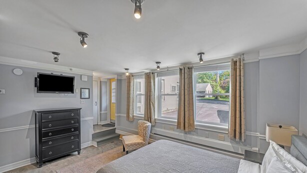 A hotel room with a bed, a dresser, a chair, a TV, and large windows with curtains.