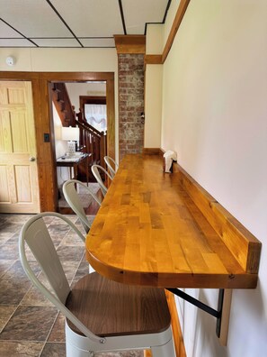 A long wooden dining table with chairs, a brick accent wall, and a staircase in the background.