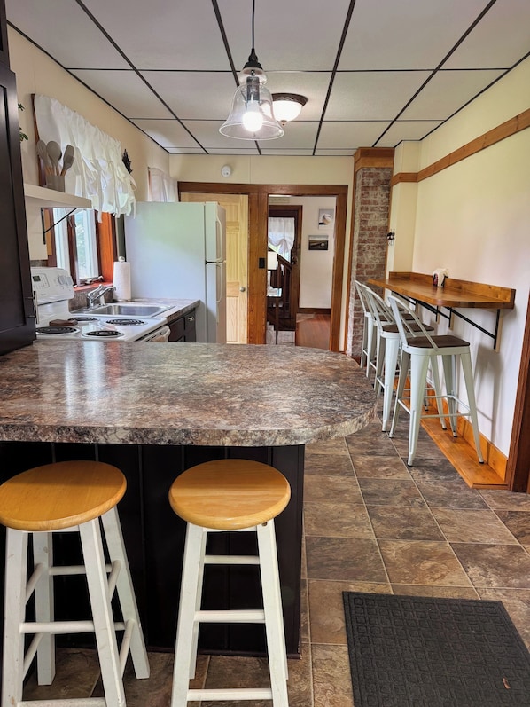A kitchen with a granite countertop, two wooden stools, a stove, and a refrigerator.