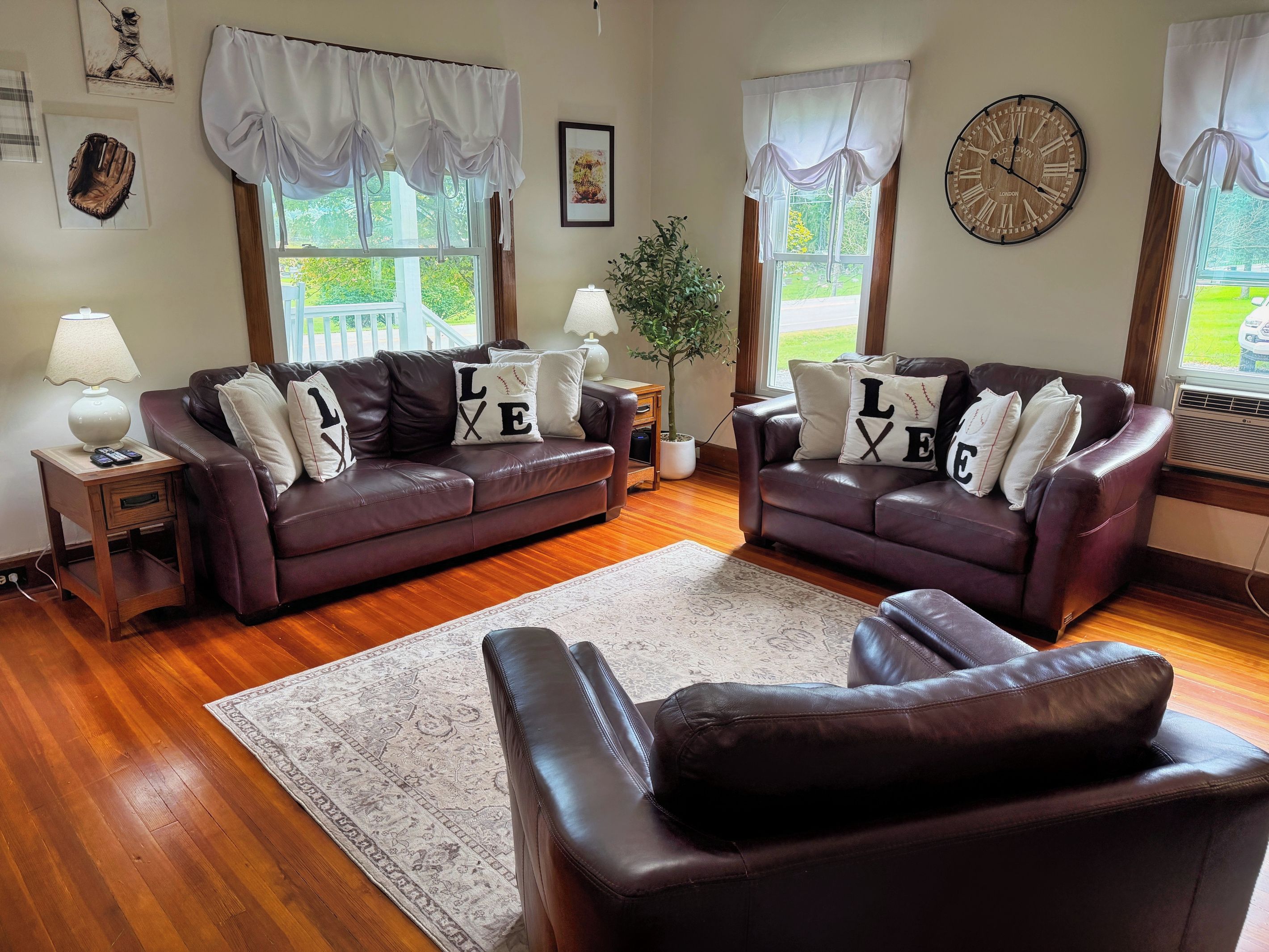 A living room with two brown leather sofas, a wooden coffee table, a white rug, and a large clock on the wall.