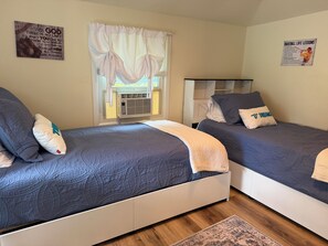 A bedroom with two beds, a window with curtains, a wall poster, and a ceiling fan. - Diamond Dreams, Very close to Dreams Park, Recent update, fire pit, large yard (Cooperstown)