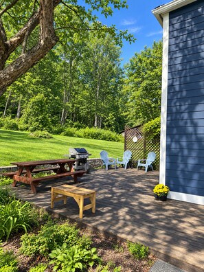 An outdoor patio with a grill, picnic table, and Adirondack chairs.