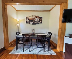 A dining area with a wooden table, four chairs, a vase with baseballs, and a wall-mounted TV. - Diamond Dreams, Very close to Dreams Park, Recent update, fire pit, large yard (Cooperstown)