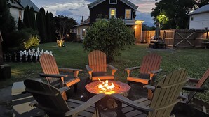 A backyard with a fire pit surrounded by four Adirondack chairs, a wooden deck, and a house in the background. - Catskill Ski Hike Lake Pet Main St Pool (Catskill)