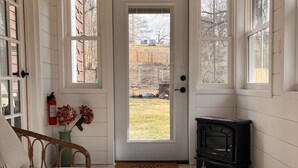 A cozy room with a wooden ceiling, a white door with a view to the outside, a small black stove, and a wicker chair. - Catskill Ski Hike Lake Pet Main St Pool (Catskill)