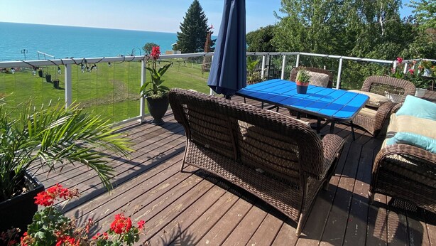 Eine Holzterrasse mit Korbmöbeln, einem blauen Tisch und Blick aufs Meer.