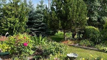 Un jardin agrémenté de diverses plantes et fleurs, une terrasse en bois et un chemin pavé de pierres.