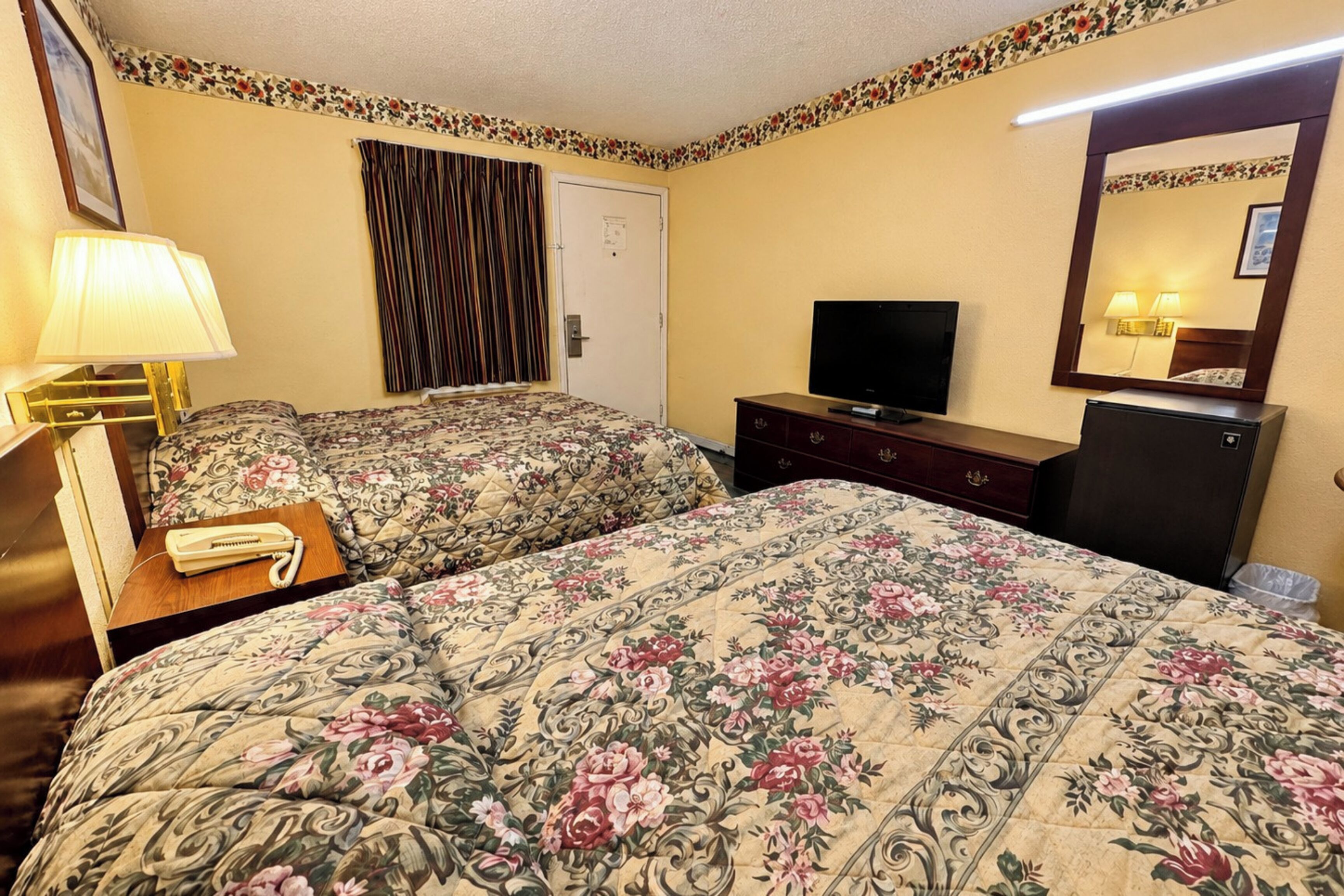 A hotel room with two beds, a television, a dresser, a lamp, and a mirror.