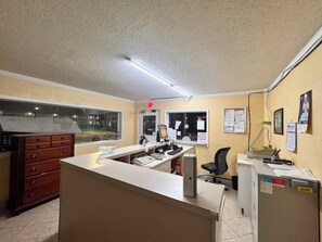 A hotel reception area with a desk, computer, telephone, and a window. - Economy Inn Sweetwater I-75 (Sweetwater)