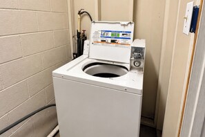 A compact, white front-loading washing machine with a control panel on top, situated in a corner of a room with beige brick walls. - Economy Inn Sweetwater I-75 (Sweetwater)
