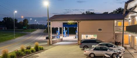 A gas station with a covered office area, multiple fuel pumps, and a parking lot with cars and a motorcycle.