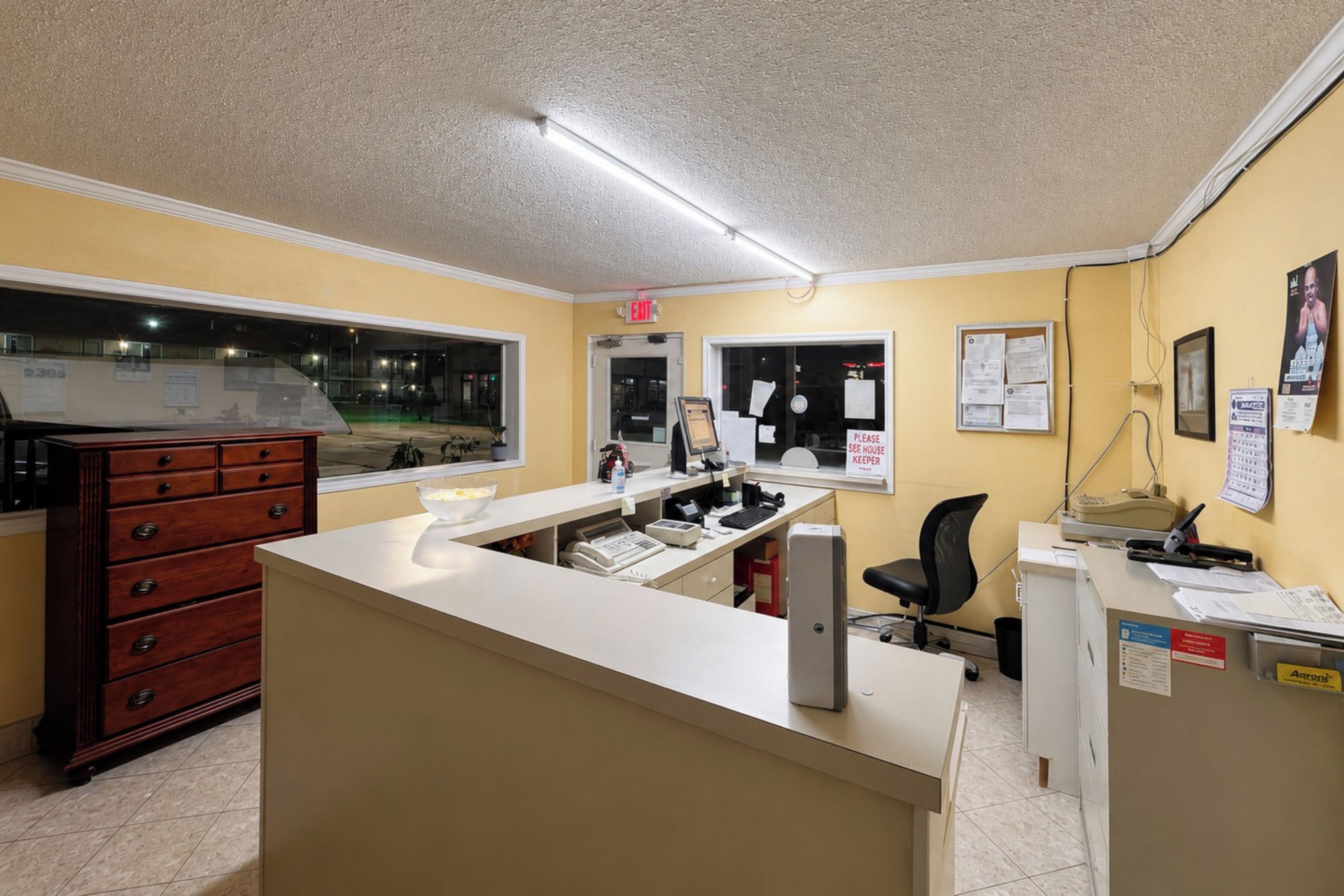 A reception desk with a computer, a telephone, and a chair. There is a window with a view of the outside.