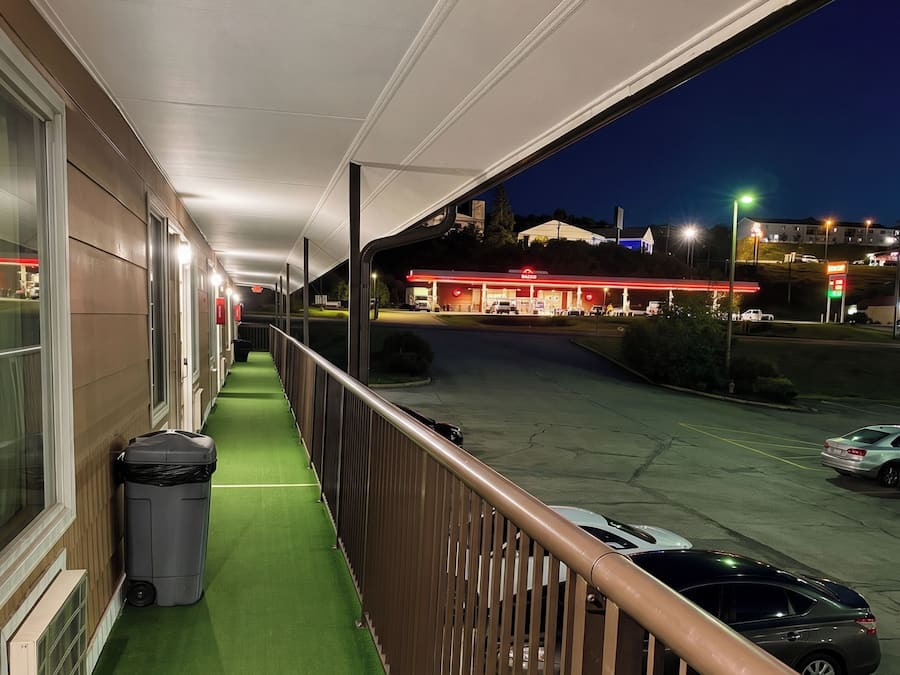 A covered outdoor corridor with a trash bin and a car parked in the background.