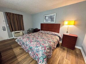 A hotel room with a bed, a bedside table, a lamp, a chair, a picture on the wall, and a window with curtains. - Economy Inn Sweetwater I-75 (Sweetwater)