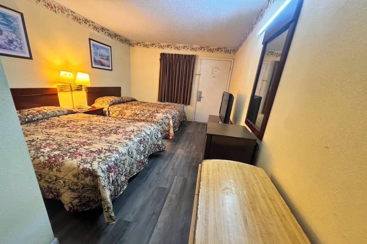 A hotel room with two beds, a desk, a chair, a television, and a door.