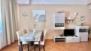 A modern living room with a dining table, chairs, a flat-screen TV, and a white cabinet with shelves. - Holiday apartment with terrace and air conditioning (Dramalj)