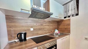 A compact kitchen with a built-in oven, a stovetop, and a microwave. There is a window with a curtain, and a wooden backsplash. - Holiday apartment with terrace and air conditioning (Dramalj)