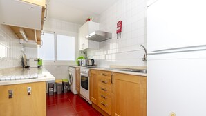 A modern kitchen with white cabinets, a stainless steel range hood, a built-in oven, and a red tiled floor. - Apartamento Watson by Mallorca North Villas (Port de Pollença)