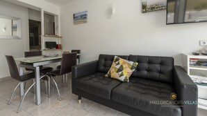 A modern living room with a black leather sofa, a dining table with chairs, and a flat-screen TV mounted on the wall. - Apartamento Watson by Mallorca North Villas (Port de Pollença)