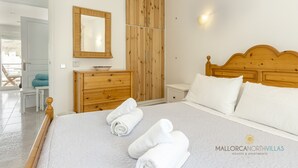A bedroom with a wooden headboard, a bed with white linens, a wooden dresser, a mirror, and a nightstand. - Apartamento Watson by Mallorca North Villas (Port de Pollença)