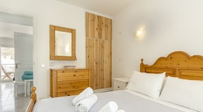 A bedroom with a wooden headboard, a bed with white linens, a wooden dresser, a mirror, and a nightstand.