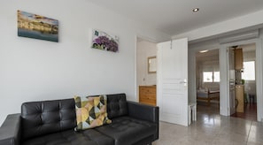 A modern living room with a black leather sofa, a wooden door leading to a kitchen, and a dining area.