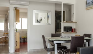 A dining area with a glass table, black chairs, a large mirror, and a kitchen in the background.