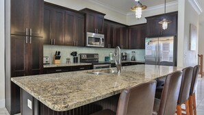 A kitchen with dark wood cabinets, stainless steel appliances, a granite countertop, and a bar stool.