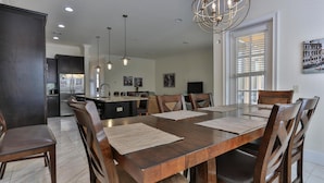 A spacious dining area with a large wooden table, multiple chairs, and pendant lighting.