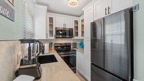 A modern kitchen with white cabinets, stainless steel appliances, and a marble countertop.