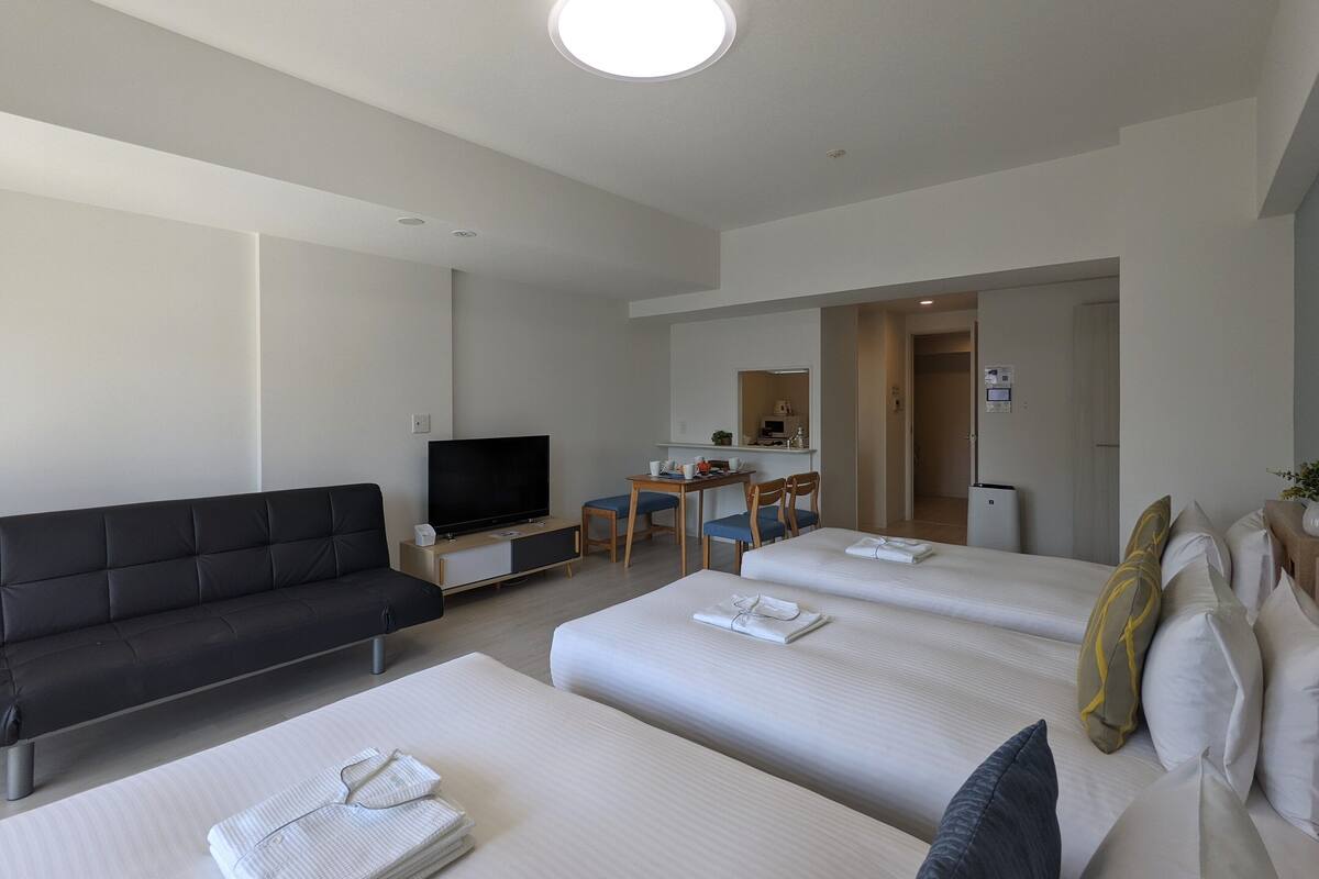 A hotel room with two beds, a sofa, a TV, a desk with a chair, and a mirror.
