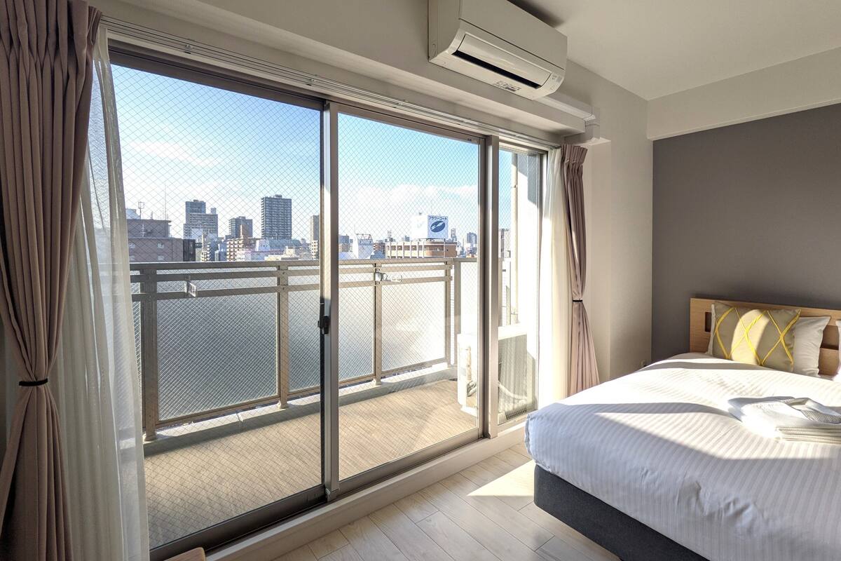 A hotel room with a large sliding glass door to a balcony, a bed with a headboard, and an air conditioning unit mounted on the wall.