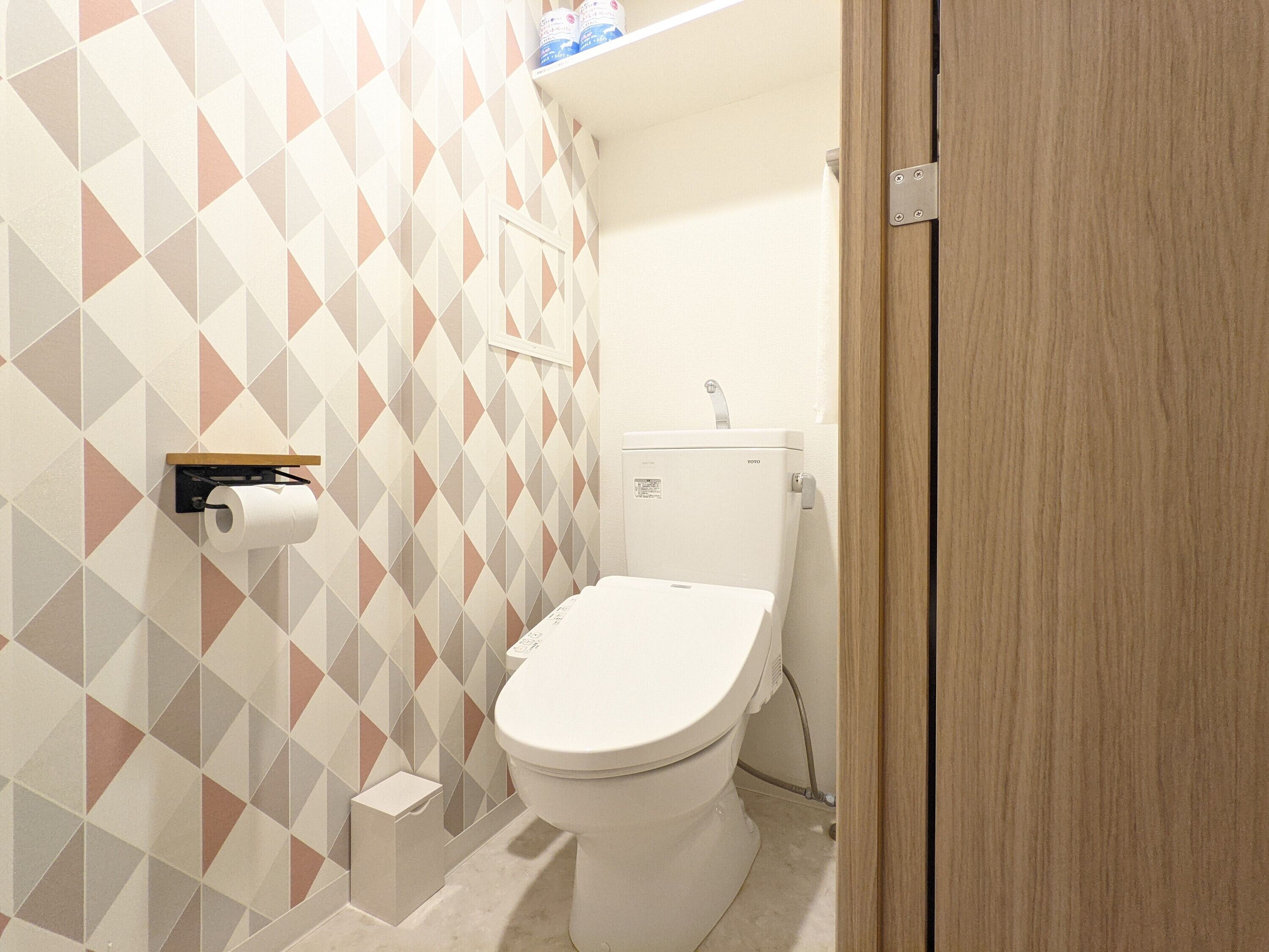 Ein Badezimmer mit Toilette, Papierhandtuchspender und einer Wandablage.