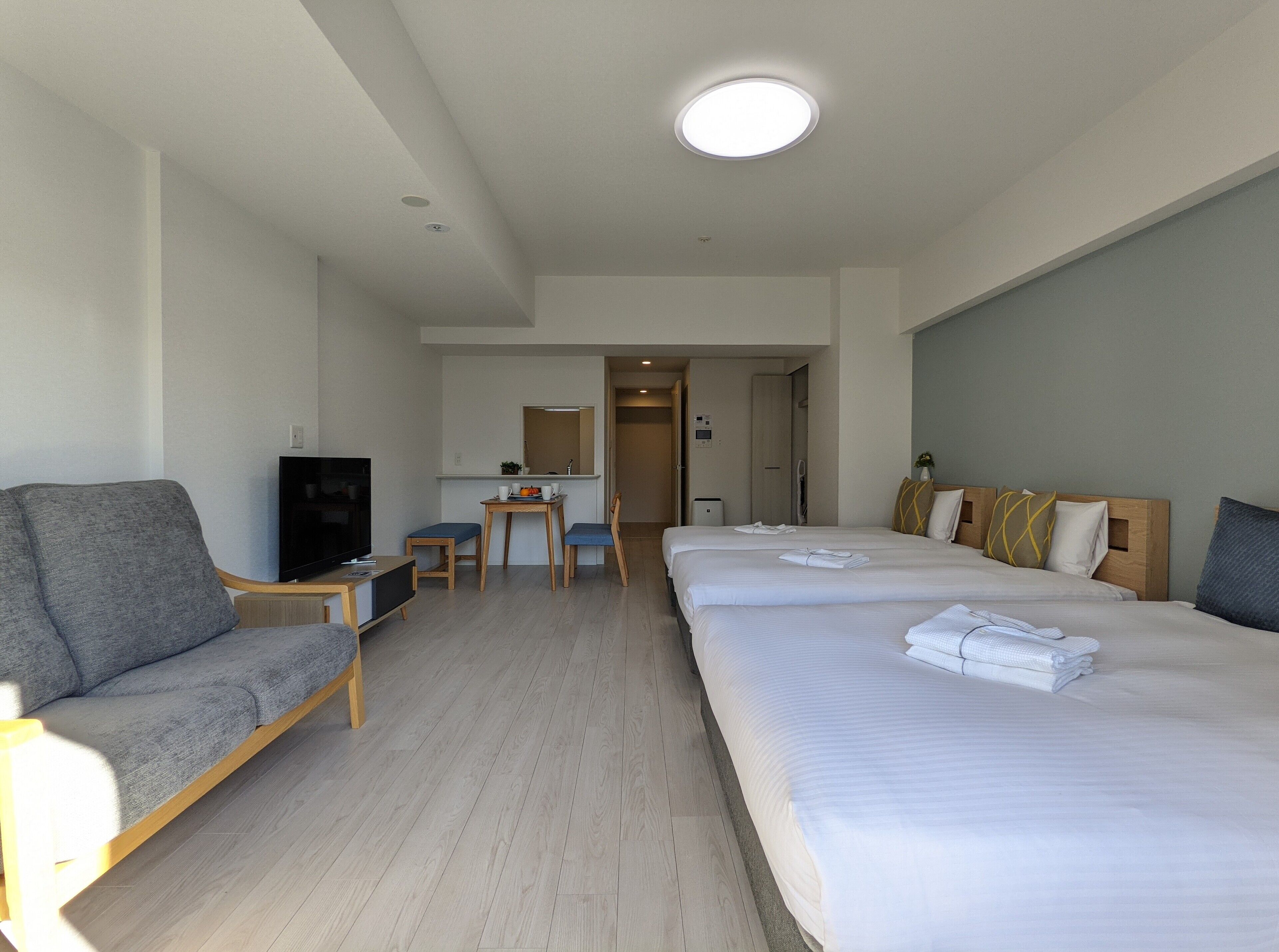 Une chambre d’hôtel équipée d’un canapé, d’une télévision, d’un bureau, de deux lits et d’une salle de bain visible à travers une porte ouverte.