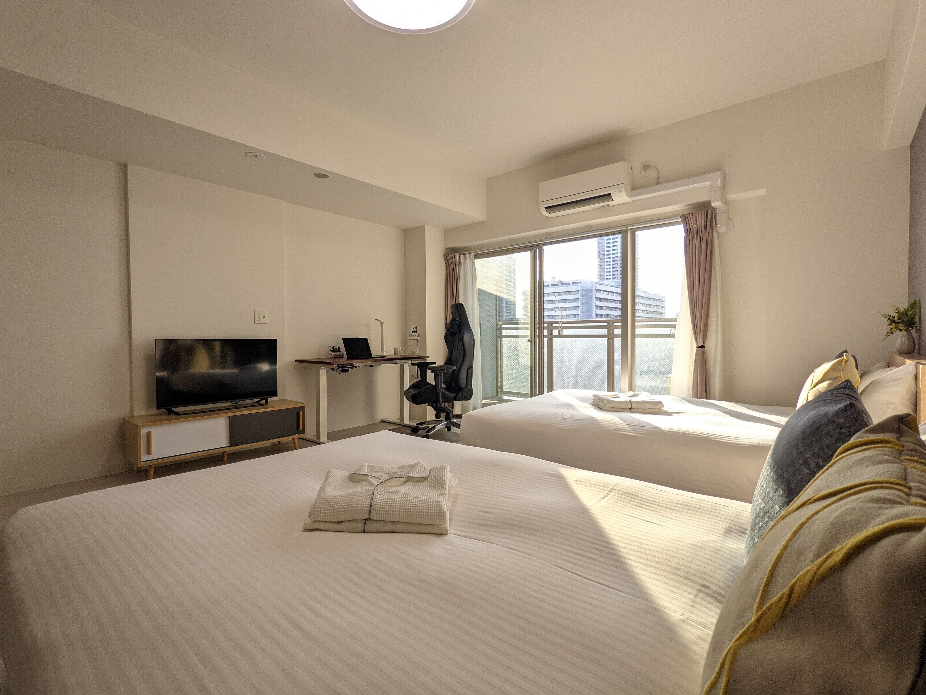 Habitación de hotel con dos camas, un escritorio con televisor y ventana con vista a la ciudad.
