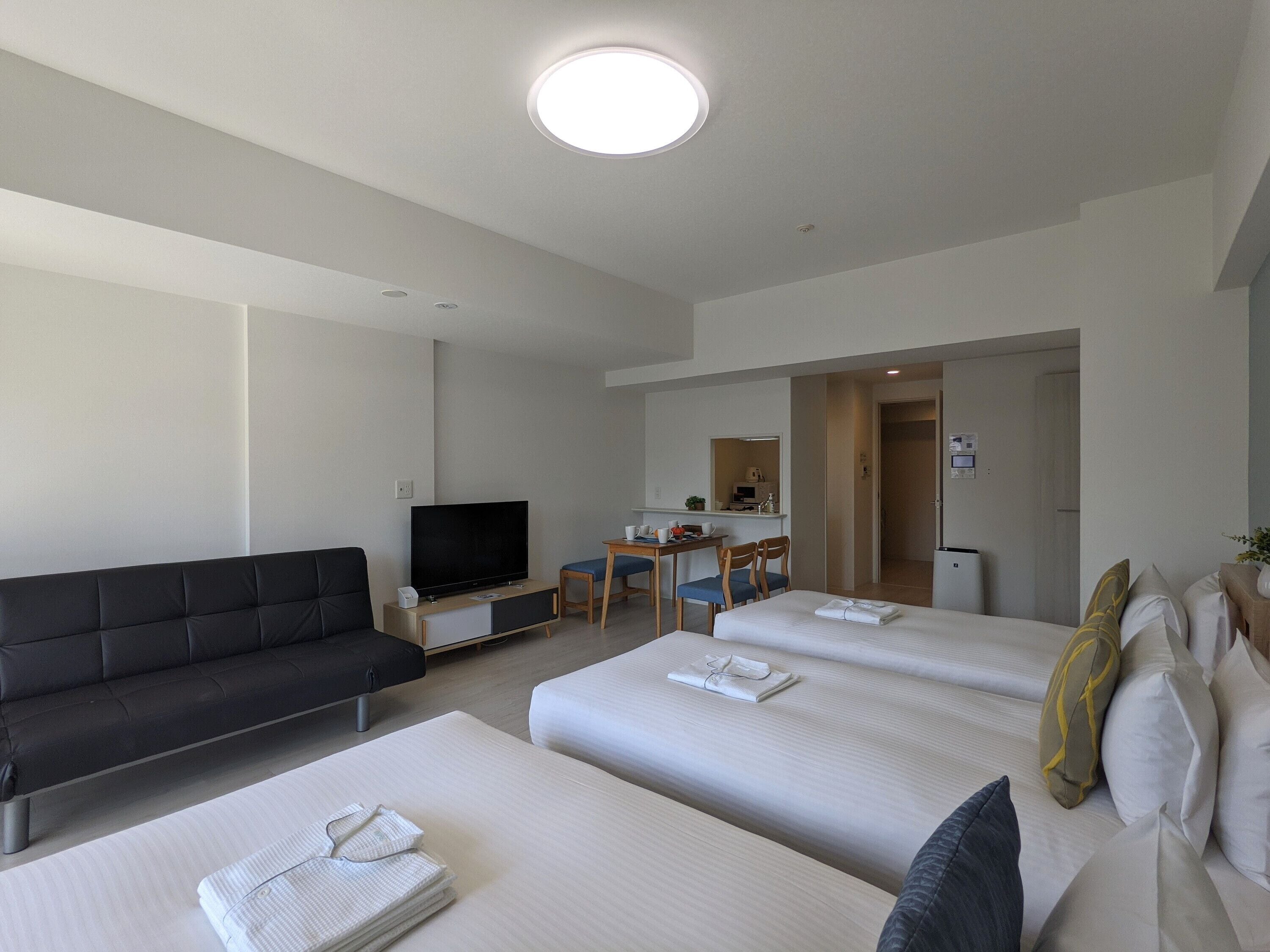 A hotel room with a sofa, a TV, a desk with chairs, and two beds.