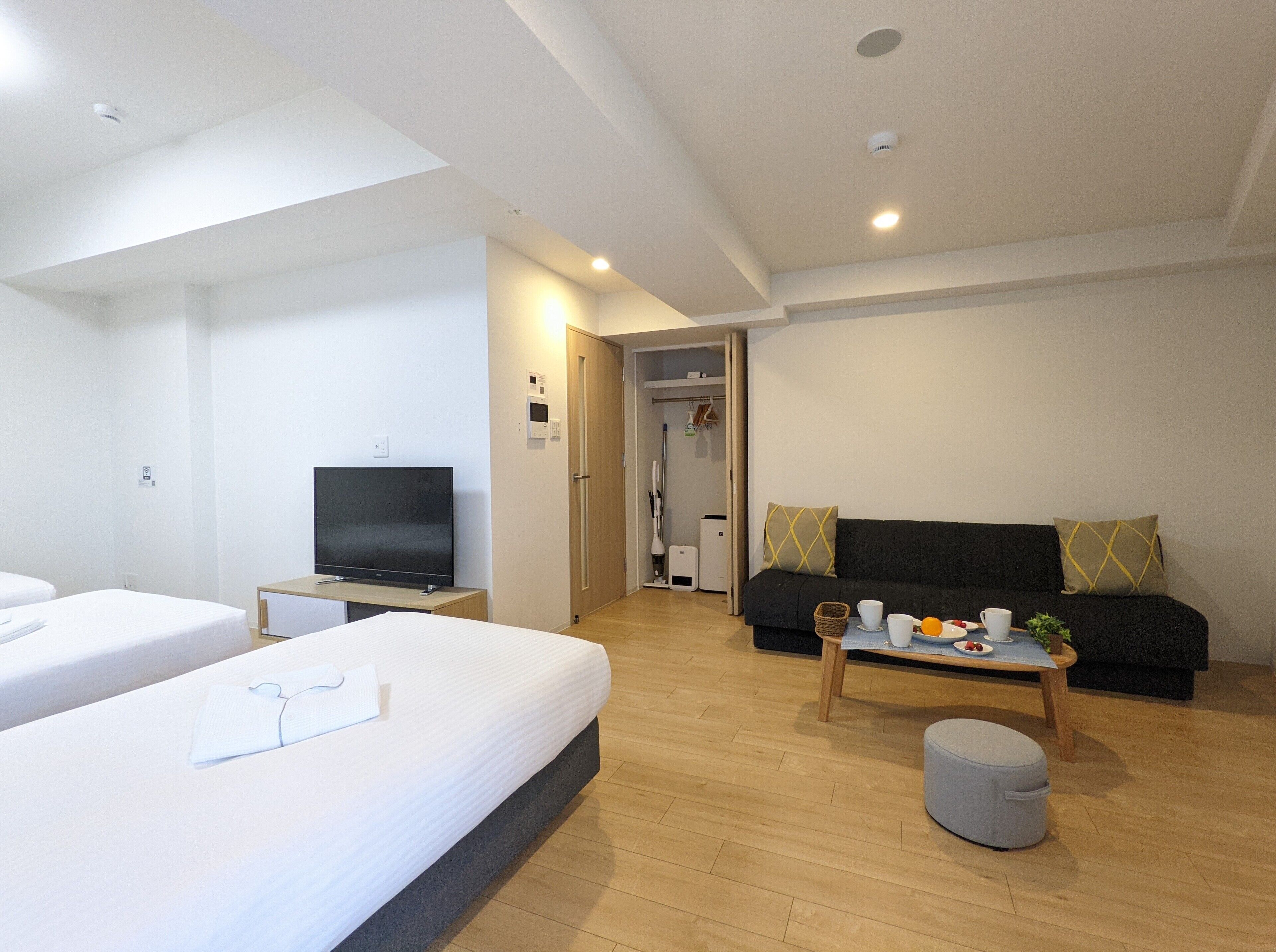 A modern hotel room with two single beds, a flat-screen TV, a sofa, a small table with a basket, and a coffee table.