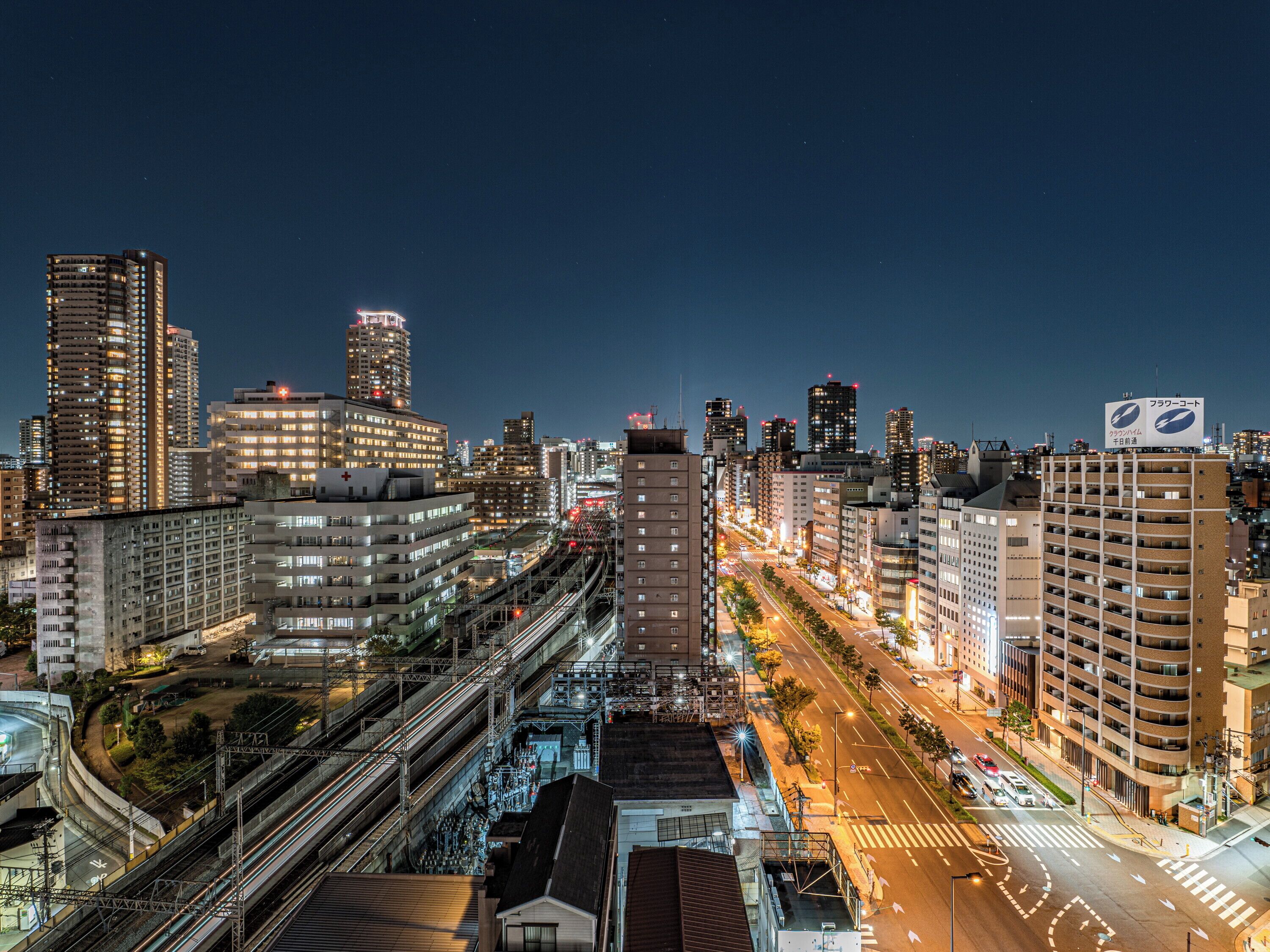 Un paisaje urbano nocturno con rascacielos, un hospital destacado y una calle concurrida con tráfico visible.