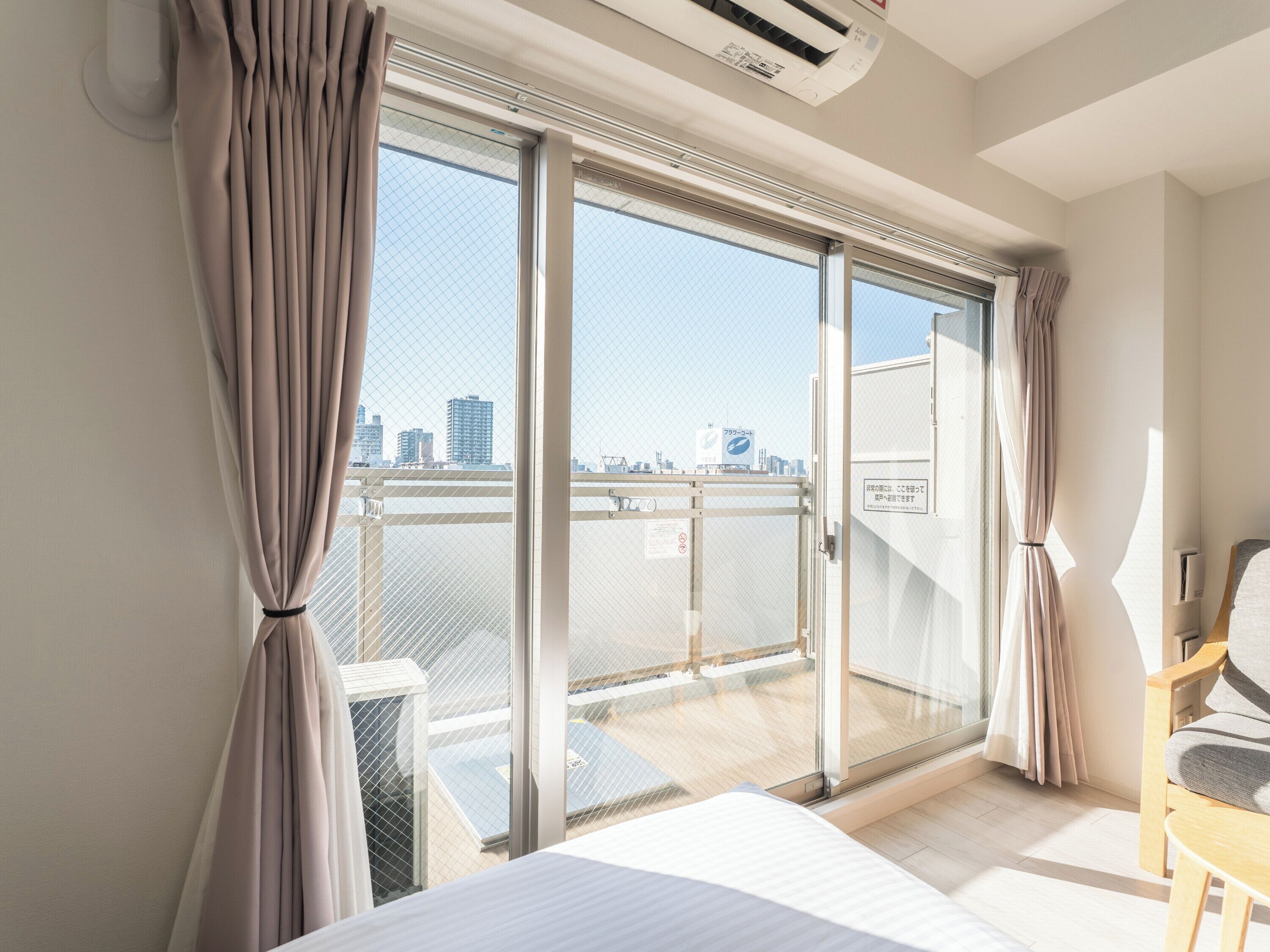 Habitación de hotel con un gran ventanal corredera a un balcón, una cama, un escritorio y una silla.