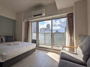 A modern hotel room with a large bed, a grey armchair, and a balcony with a city view. - ESLEAD HOTEL OSAKA TSURUHASHI (Osaka)