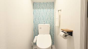 Une petite salle de bain comprenant des toilettes, un porte-rouleau de papier toilette et une étagère avec des articles de toilette.
