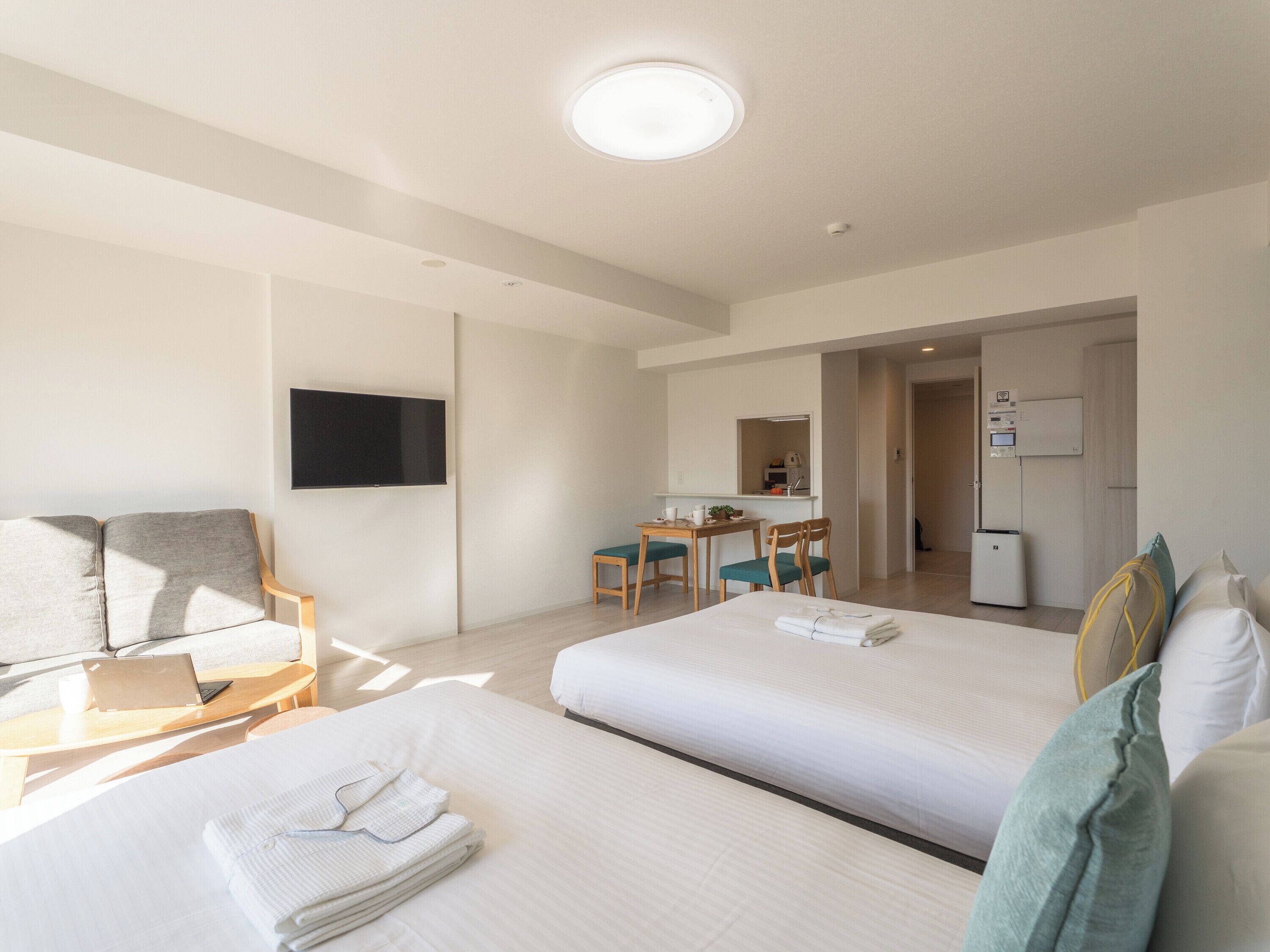 A hotel room with two beds, a desk with a chair, a flat-screen TV mounted on the wall, and a refrigerator.