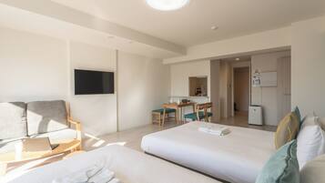 A hotel room with two beds, a desk with a chair, a flat-screen TV mounted on the wall, and a refrigerator.