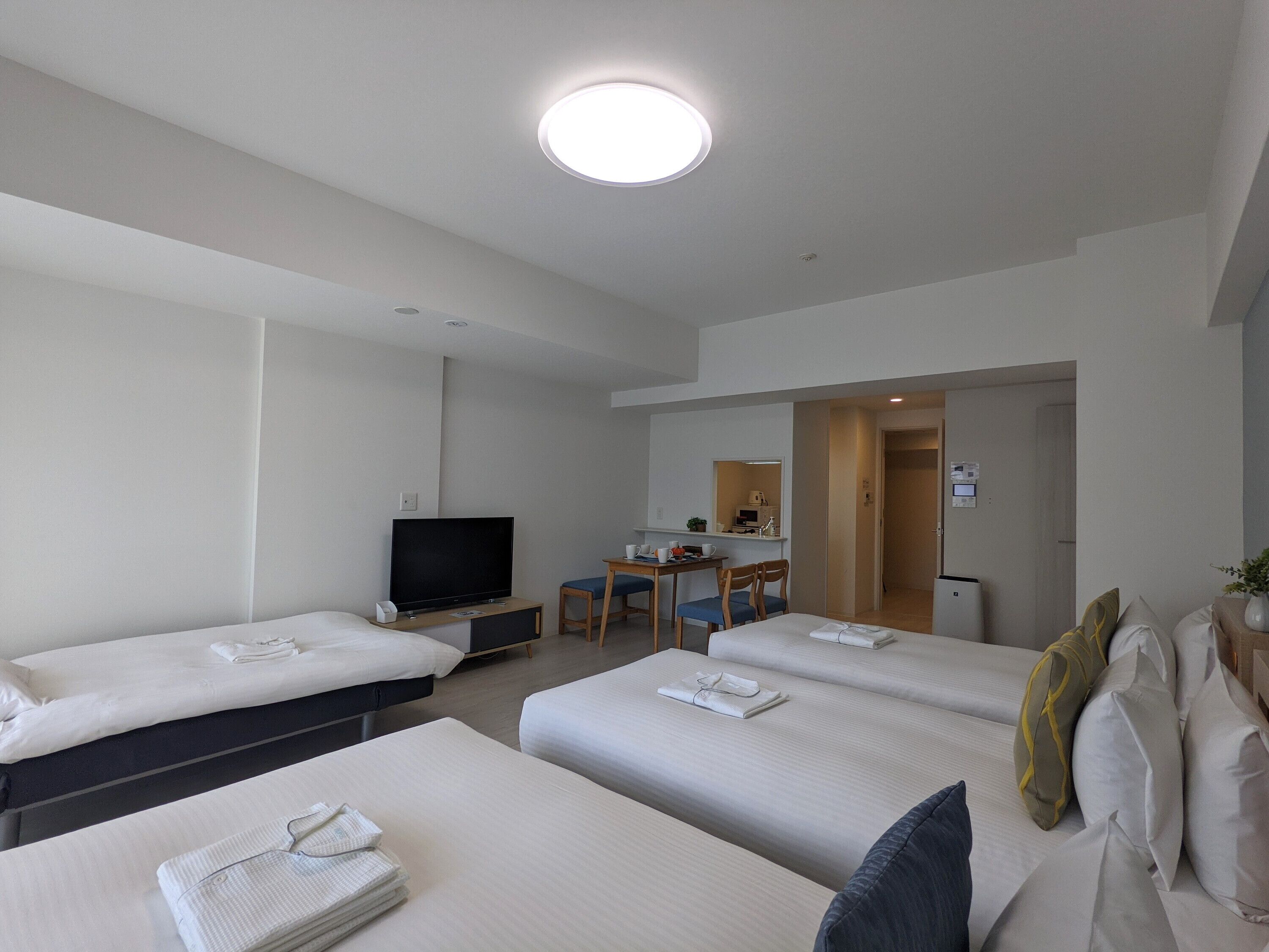 A hotel room with two beds, a television, a desk with a chair, and a kitchenette.