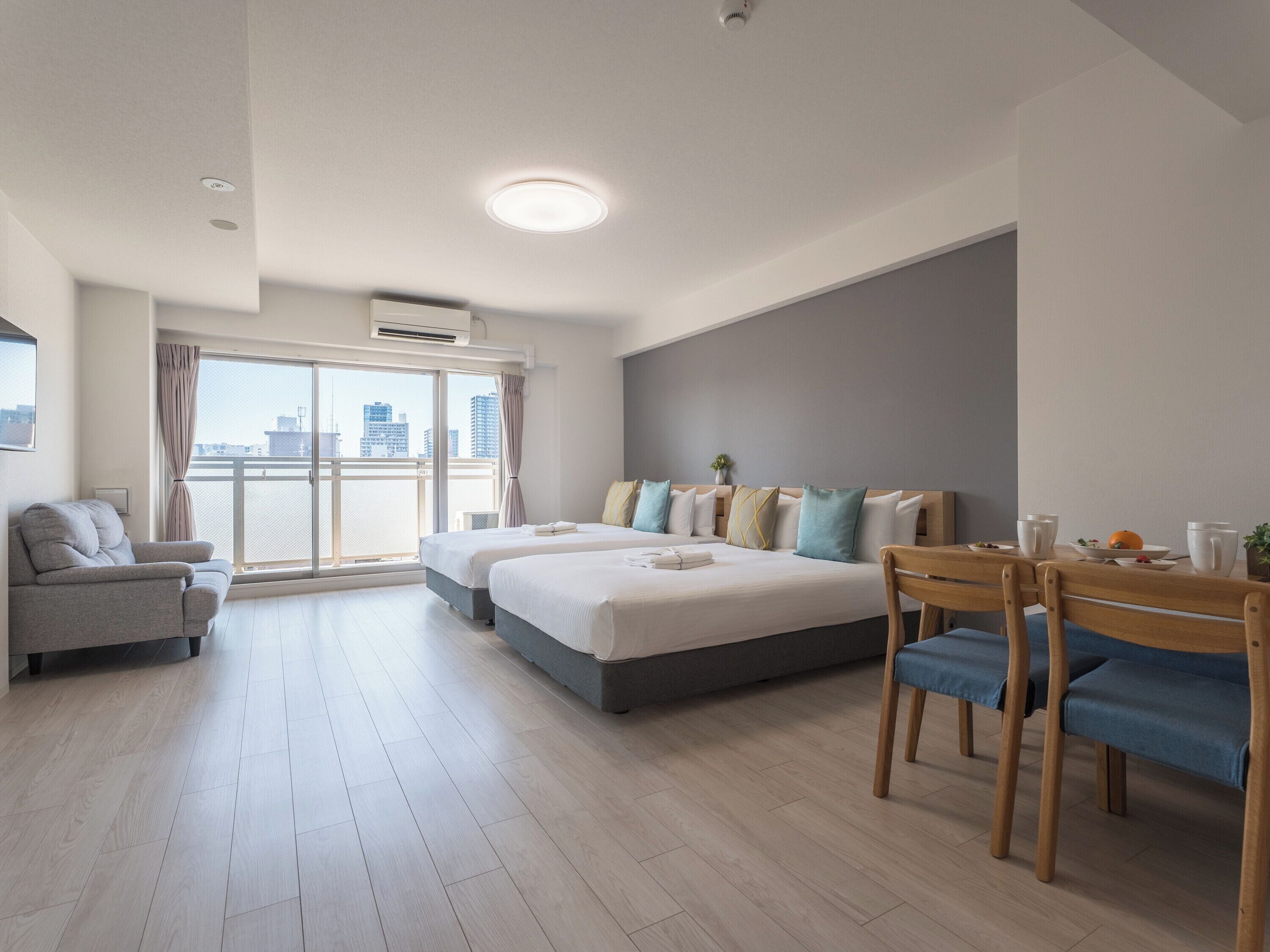Quarto de hotel moderno com varanda, área de refeições e uma cama grande com várias almofadas.